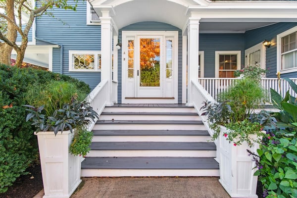 Front entrance with white arched portico, dark gray deck stairs, white railings, and potted plants flanking the white front door